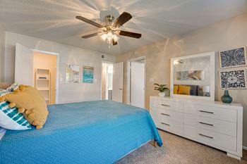 A bedroom with a blue bedspread and a white dresser.